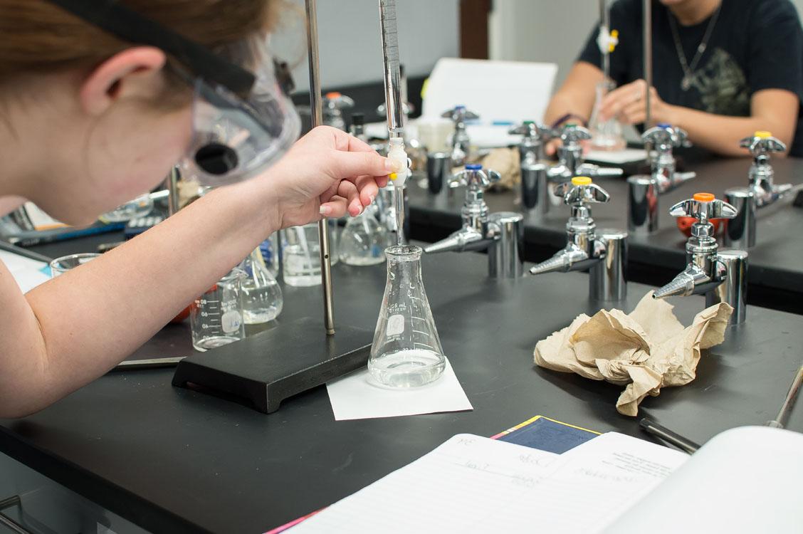 Student in chemistry lab looking at flask.