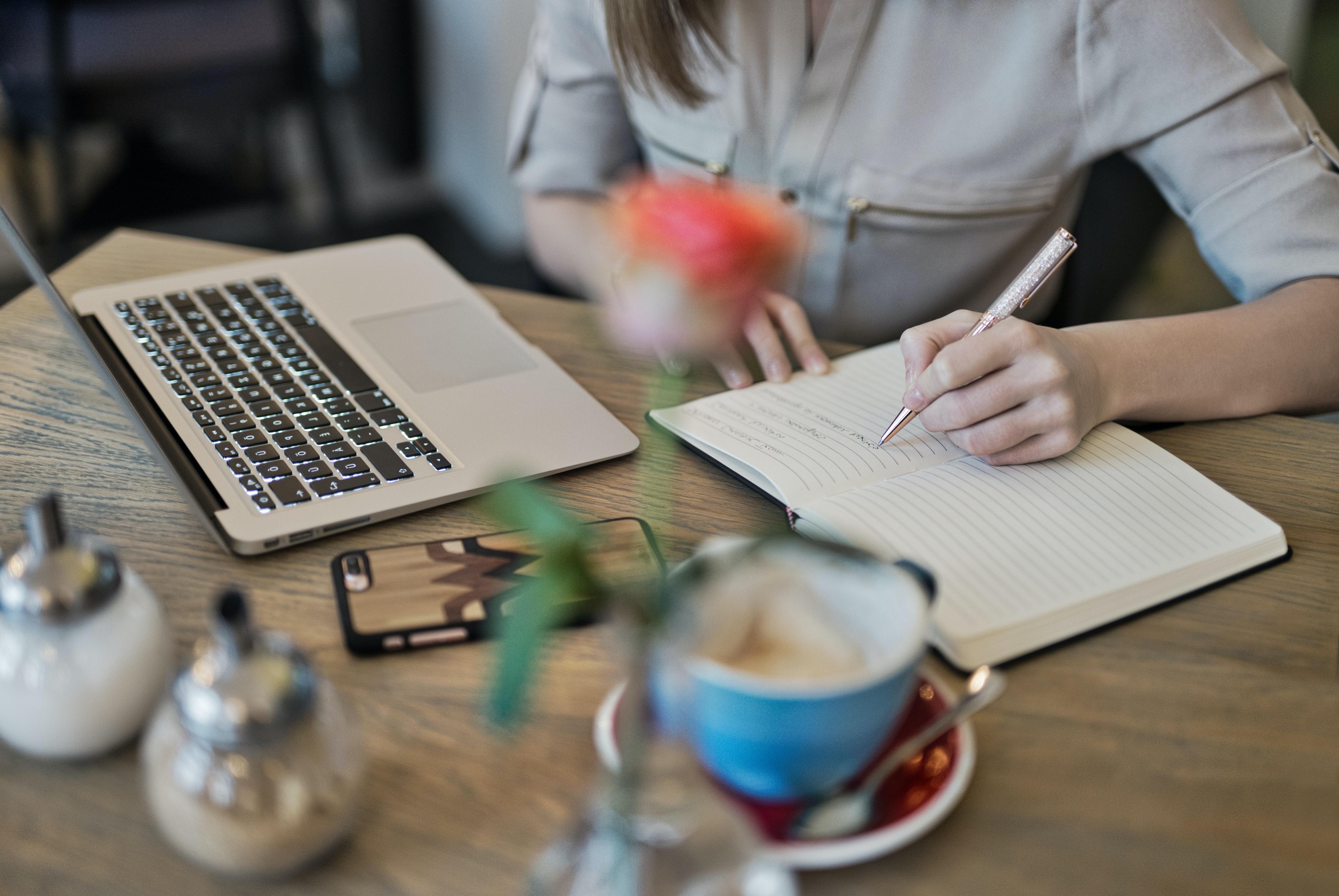 Female student writing notes from her notebook onto her computer